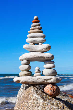 High pyramid of white stones balance on the edge of the cliff on the sea background. Concept of harmony and balanceの写真素材