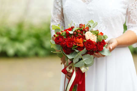 Beautiful wedding bouquet of red roses and red Hypericum berries in hands of bride. Soft focus, selective focusの写真素材