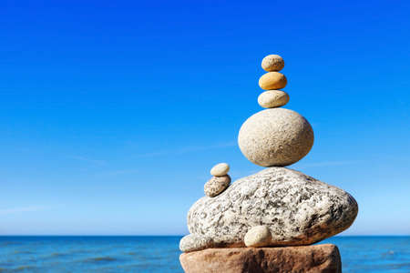 Rock zen pyramid of white and pink stones on a background of blue sky and sea. Concept of balance,...