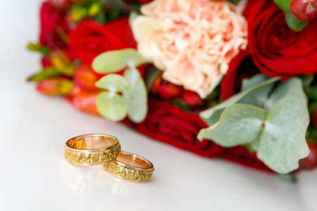 Gold wedding rings on a white background and a bouquet of a bride from roses. Soft focus, selective focusの写真素材