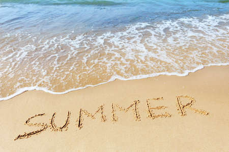 The word "Summer" written on the sand at the edge of the sea. The concept of summer vacation and good moodの写真素材