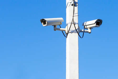 two CCTV cameras mounted on a pole on the background of blue skyの写真素材