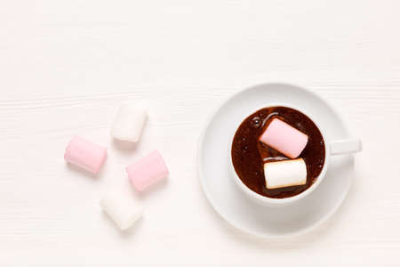 White Cup with coffee and white and pink marshmallow on wooden table. Top view