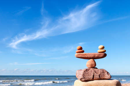 Symbolic scales of stones on the background of the sea and blue sky. Concept of life balance and harmony. Pros and cons conceptの写真素材