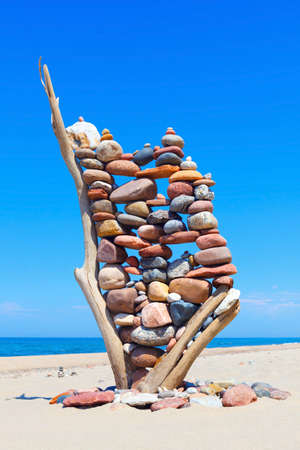 stack of multicolored balanced stones on an old wooden snags, on a blue sky and sea background....