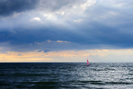 small boat with a sail on the sea under the stormy skyの写真素材