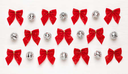 Christmas pattern of red bows and mirror balls on white wooden background. Flat lay, top view