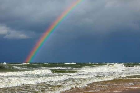 Bright rainbow on the background of storm clouds over the raging seaの写真素材