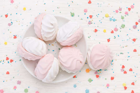 White and pink marshmallow (zephyr) and Multicolored Sugar sprinkle dots on a wooden table. Top view