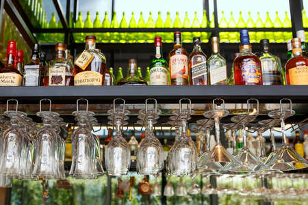 Singapore, Singapore-November 28, 2019: Wine glasses hang over the bar counter on the background of bottles with alcoholic drinks. Soft focus, selective focusのeditorial素材