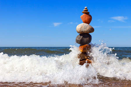 Rock zen pyramid of colorful pebbles standing in the water on the background of the sea and waves. Concept of balance, harmony and meditationの写真素材