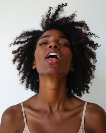 A young woman with dark skin and curly hair laughs with her eyes closed and mouth open, showing her white teeth and relaxed facial expression.の素材