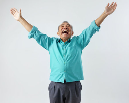 Elderly Asian man with gray hair, wearing a teal shirt, shouting with arms raised in frustration or anger, displaying a mix of intense emotion and desperation.の素材