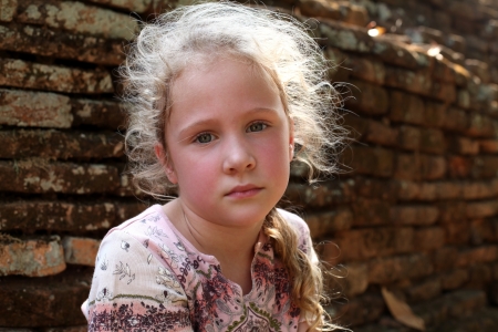 sad little girl on the background of an old brick wallの写真素材