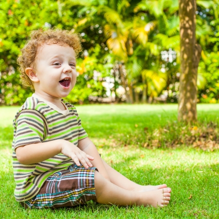 happy little boy sitting on the grass in the gardenの写真素材