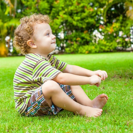 happy little boy sitting on the grass in the gardenの写真素材
