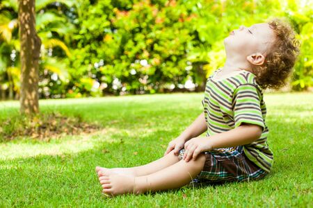 happy little boy sitting on the grass in the gardenの写真素材