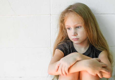 sad little girl sitting near the wallの写真素材