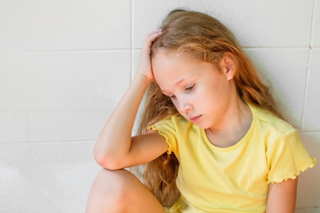 sad little girl sitting near the wallの写真素材