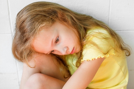 sad little girl sitting near the wallの写真素材