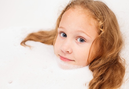 Cute eight year old girl taking a relaxing bath with foam. The symbol of purity and hygiene education.の写真素材