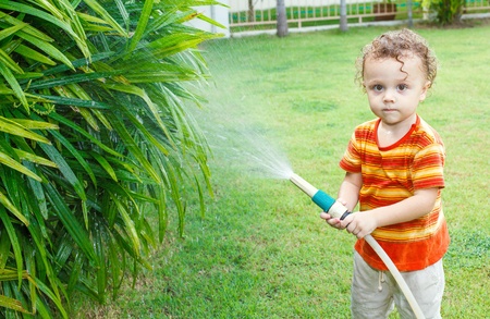 Happy little boy pours water from a hoseの写真素材
