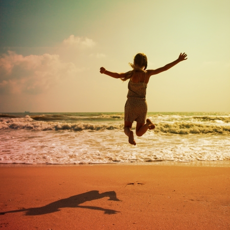 Happy girl jumping on the beach on the dawn timeの写真素材