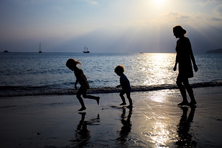 Mother and two kids silhouettes running on beach at sunset の写真素材