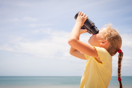 little girl on the beach looking at the sky through binocularsの写真素材