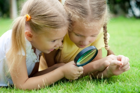 Two little girls with magnifying glass outdoors in the day timeの写真素材