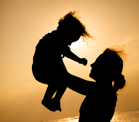 Mother and little son silhouettes on beach at sunsetの写真素材