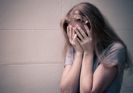 one sad woman sitting on the floor near a wall and holding her head in her handsの写真素材