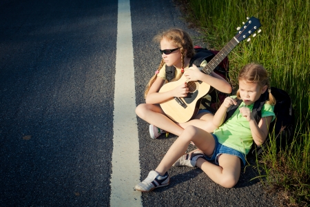 two girls with backpacks sitting on the roadの写真素材