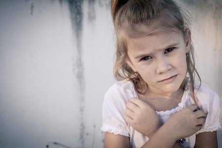 Portrait of sad little girl sitting near  wall in the day time