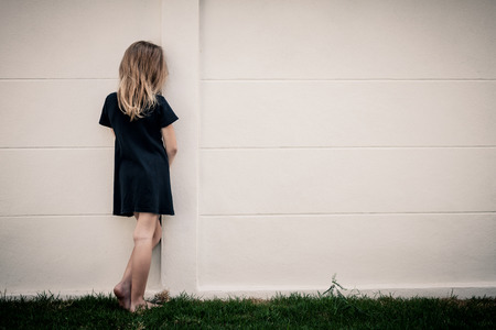 Portrait of sad little girl standing near wall in the day timeの写真素材
