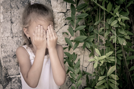 Portrait of sad little girl standing near stone wall in the day timeの写真素材