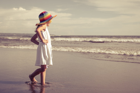Happy little girl in the hat walking at the beach in the day timeの写真素材