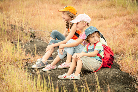 three little kids with backpack sitting on the footpath in the mountainsの写真素材