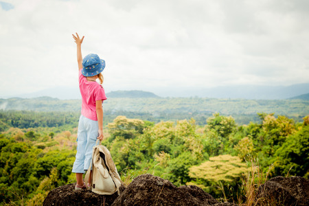little girl with a backpack on a mountain topの写真素材