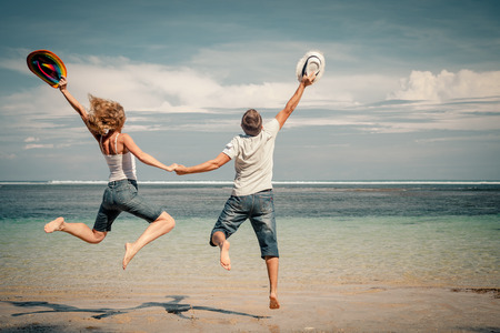 happy couple jumping on the beach at the day timeの写真素材