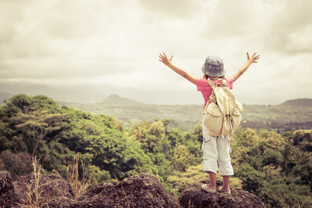 little girl with a backpack standing on a mountain top at the day timeの写真素材