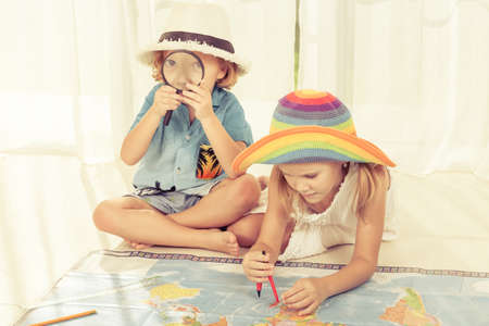 brother and sister are considering a world map with a magnifying glass at homeの写真素材