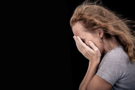 portrait of one sad woman standing near a wall and holding her head in her handsの写真素材