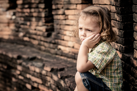 Portrait of sad little boy sitting near the wall at the day timeの写真素材