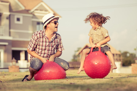 Dad and son jumping on inflatable balls on the lawn in front of house at the day timeの写真素材