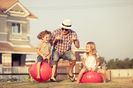 Dad, son and daughter jumping on inflatable balls on the lawn in front of house at the day timeの写真素材
