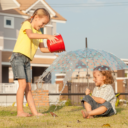 brother and sister playing with water near a house at the day timeの写真素材