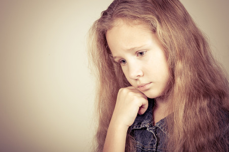 Portrait of sad blond teen girl standing near wall