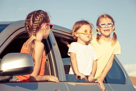 Happy brother and his two sisters are sitting in the car at the day timeの写真素材