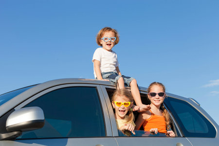 Happy brother and his two sisters are sitting in the car at the day timeの写真素材